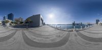 360 - fisheye lens photograph of an oceanfront, with a body of water and a city in the background