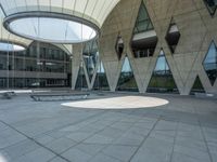 the empty courtyard with two benches is shown outside of a large building with glass walls