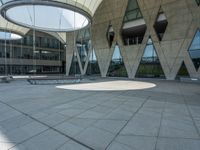 the empty courtyard with two benches is shown outside of a large building with glass walls