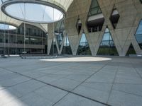 the empty courtyard with two benches is shown outside of a large building with glass walls