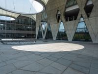 the empty courtyard with two benches is shown outside of a large building with glass walls