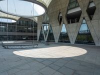 the empty courtyard with two benches is shown outside of a large building with glass walls