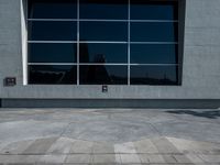 a man riding a skateboard down the side of a sidewalk near a building with a tall window