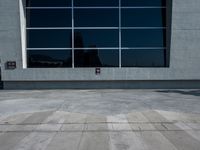 a man riding a skateboard down the side of a sidewalk near a building with a tall window