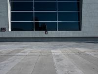 a man riding a skateboard down the side of a sidewalk near a building with a tall window