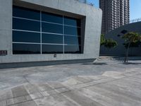 a skateboard sits on the cement pavement outside of a building next to a tree