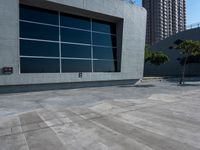 a skateboard sits on the cement pavement outside of a building next to a tree