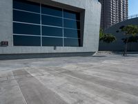 a skateboard sits on the cement pavement outside of a building next to a tree