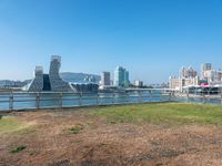 an empty grassy field next to a marina filled with lots of tall buildings on a clear day