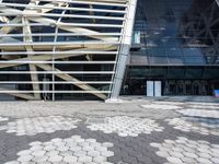 the outside view of a glass and steel building, from which a large, white lattice like structure has been arranged over a street with tiles