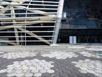 the outside view of a glass and steel building, from which a large, white lattice like structure has been arranged over a street with tiles