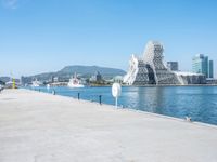 a man sitting on his bike near a waterway with water in the background, and some buildings by the shore