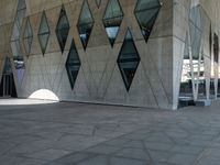 an empty stone sidewalk with large glass windows on one side and a white building on the other