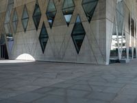 an empty stone sidewalk with large glass windows on one side and a white building on the other