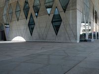 an empty stone sidewalk with large glass windows on one side and a white building on the other