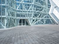 a stone paved sidewalk and an outdoor courtyard with a tall building with a glass facade