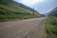 a dirt road and a hill side with trees on either side of it and a cloudy blue sky overhead