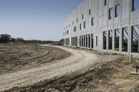 this is a construction site where a gravel road is going into a large building with lots of windows
