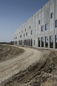 this is a construction site where a gravel road is going into a large building with lots of windows
