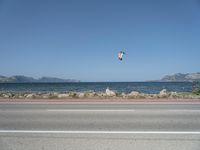 kites fly over the beach with a distant lake and mountains in the background from a highway