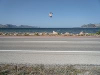 kites fly over the beach with a distant lake and mountains in the background from a highway