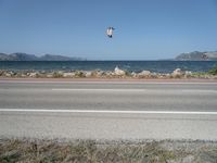 kites fly over the beach with a distant lake and mountains in the background from a highway