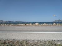 kites fly over the beach with a distant lake and mountains in the background from a highway