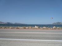 kites fly over the beach with a distant lake and mountains in the background from a highway