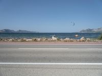 kites fly over the beach with a distant lake and mountains in the background from a highway