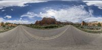 a wide angle shot of a road and mountain under blue skies with clouds and sun