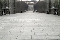 large concrete city square with many pedestrians and pedestrians walking down stairs with trees in back