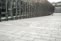 a stone sidewalk between two tall glass buildings next to stairs and staircases, with stairs in front