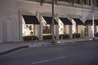 a black and white restaurant with palm trees on the sidewalk in front of it at night