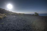 a blue sky above a dirt path and a hill by the water with bright sun