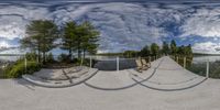 a 360 - view photo of a bench at the edge of a pier on a lake