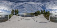 a 360 camera lens showing the path in front of some lake area with trees and clouds