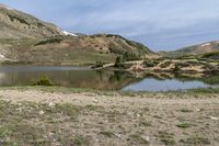 a mountain has a small lake in the foreground and some snow capped mountains behind it