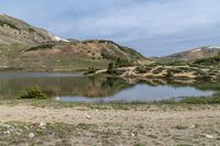 a mountain has a small lake in the foreground and some snow capped mountains behind it