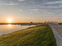 a sunset is behind a grassy shoreline by the water with a bench that looks like it has been taken down