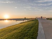 a sunset is behind a grassy shoreline by the water with a bench that looks like it has been taken down