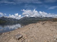 a lake with rocks on the shore and mountains in the background along side it and snow capped hills