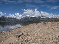 a lake with rocks on the shore and mountains in the background along side it and snow capped hills