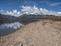 a lake with rocks on the shore and mountains in the background along side it and snow capped hills