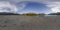 the view of a lake near mountains and some sky above it from the shore of the beach