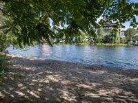 a lake in a residential area surrounded by trees and buildings, some water and people walking along the shoreline