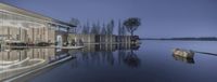 a lake side house sits next to the shore of the river at dusk, reflecting a glass roof