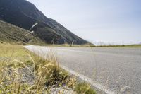 a motorcycle is on the side of a road with a mountain in the background near the grass