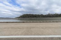 a fence in an empty parking lot overlooking water and trees of some type that is not native