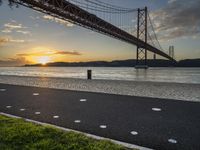 the golden hour lights up the sky near a long bridge over the water and a small area with squares on the ground in front