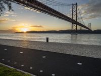 the golden hour lights up the sky near a long bridge over the water and a small area with squares on the ground in front